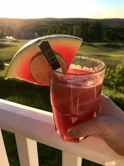 اسموتی انرژی زا خانگی هندوانه و عصاره قهوه در لیوان در دست مرد یک قاشق داخل آن هاست و با یک قاچ هندوانه و یک پر لیمو ان را تزیین کرده است. لیوان در دست قرار داد و فضای بیرون از ساختمان را نشان می دهد